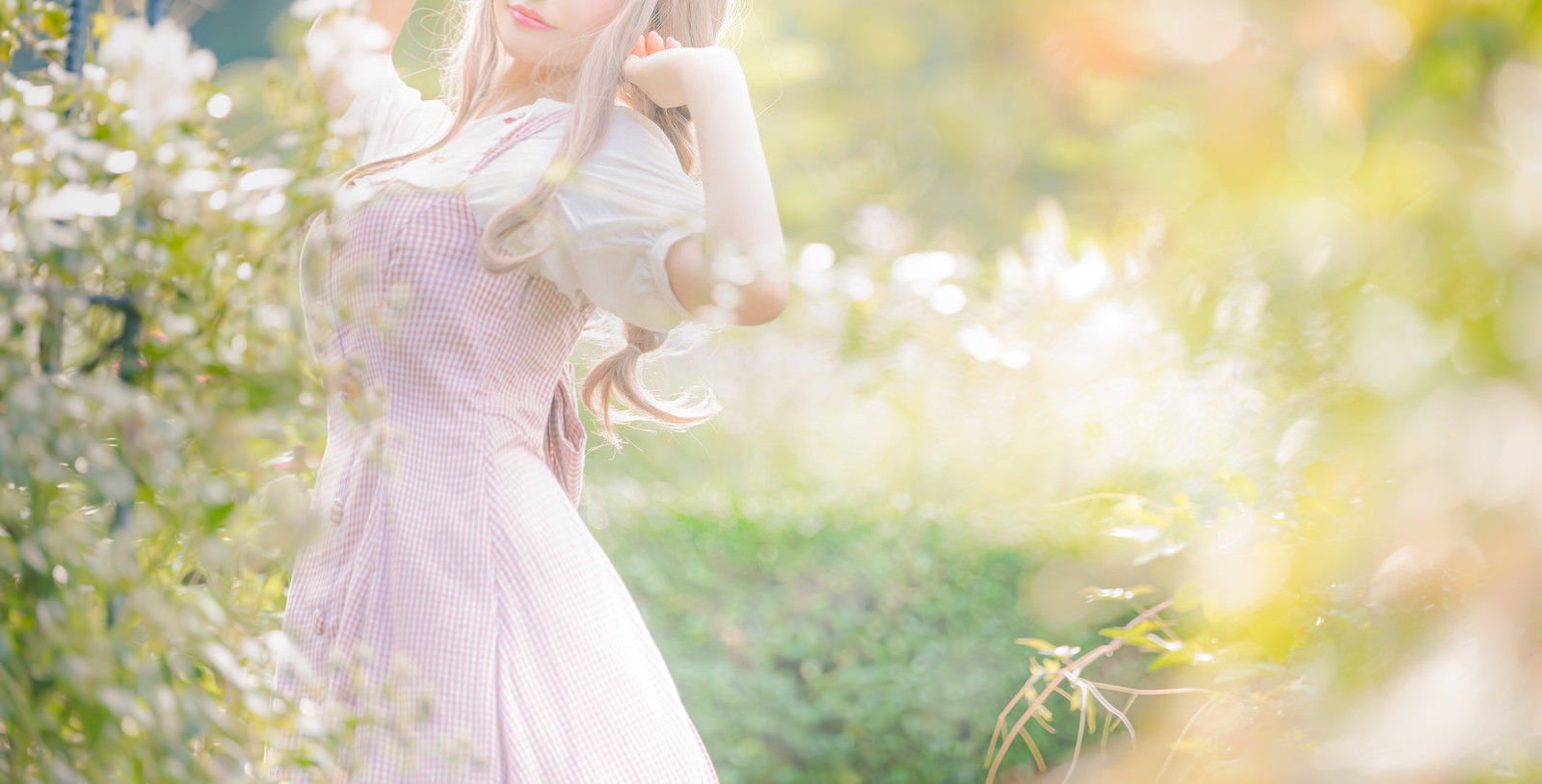 木漏れ日の中でピンクのワンピースを着た女性が庭に立つ様子［モデル：石投げて美奈代］