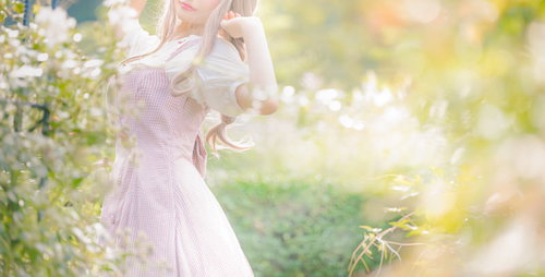 淡いピンクのワンピース姿で木漏れ日に包まれる森ガール女性