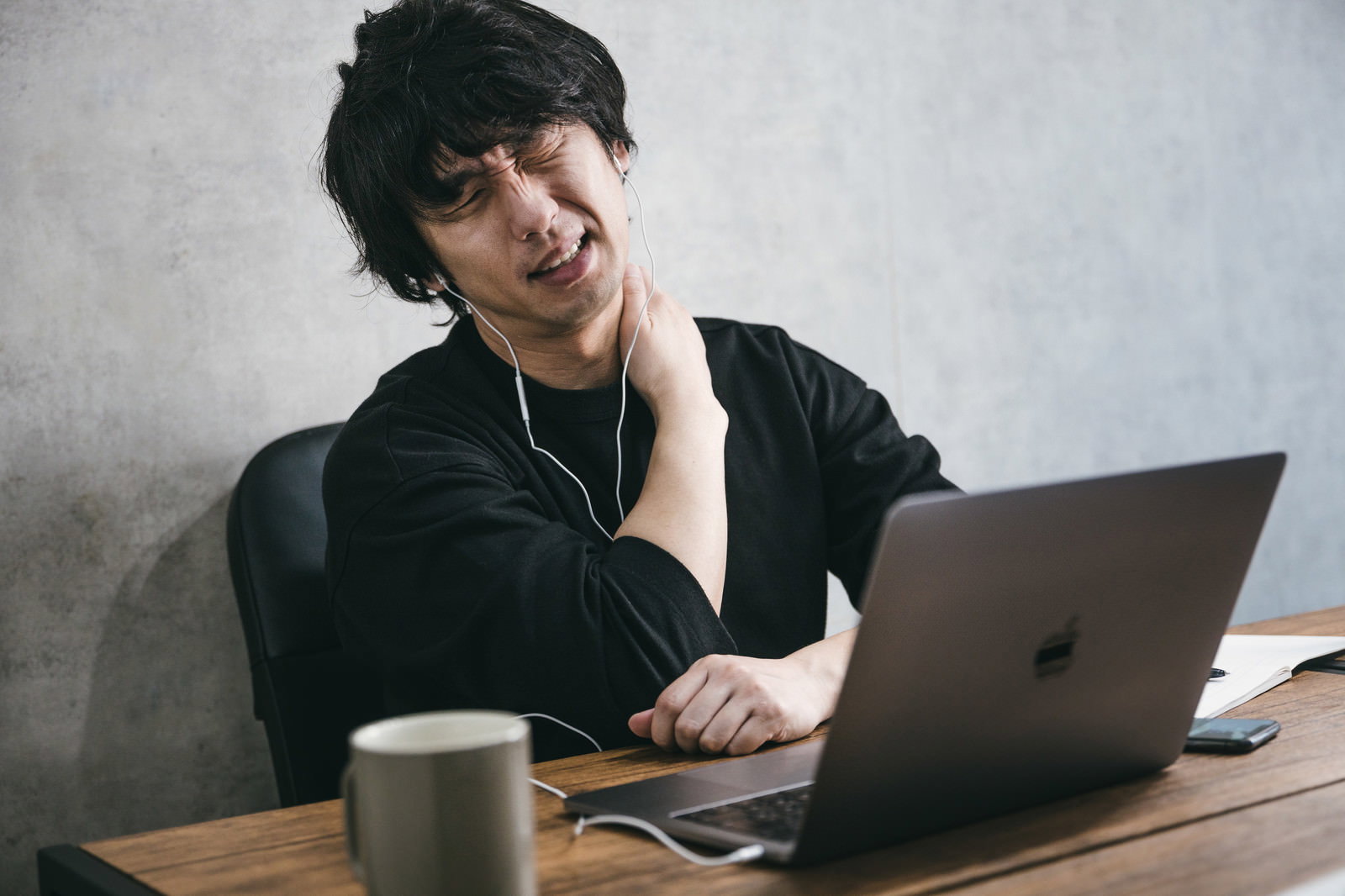 在宅勤務中に肩こりで首に手を当てて疲れた様子の男性［モデル：大川竜弥］