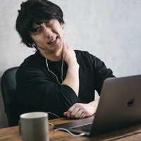 慣れない在宅勤務で肩が凝る男性、デスクワークの疲労の写真