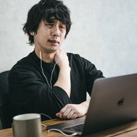 デスクワークが続いて肩こりがひどい男性がノートパソコンで作業しているの写真