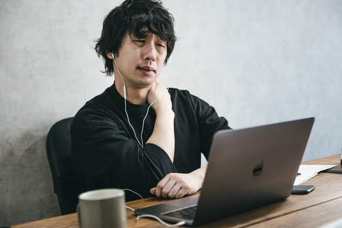 デスクワークが続いて肩こりがひどい男性がノートパソコンで作業している