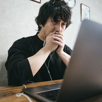 年収を見てショックを受けた男性（パソコン・イヤホン）の写真
