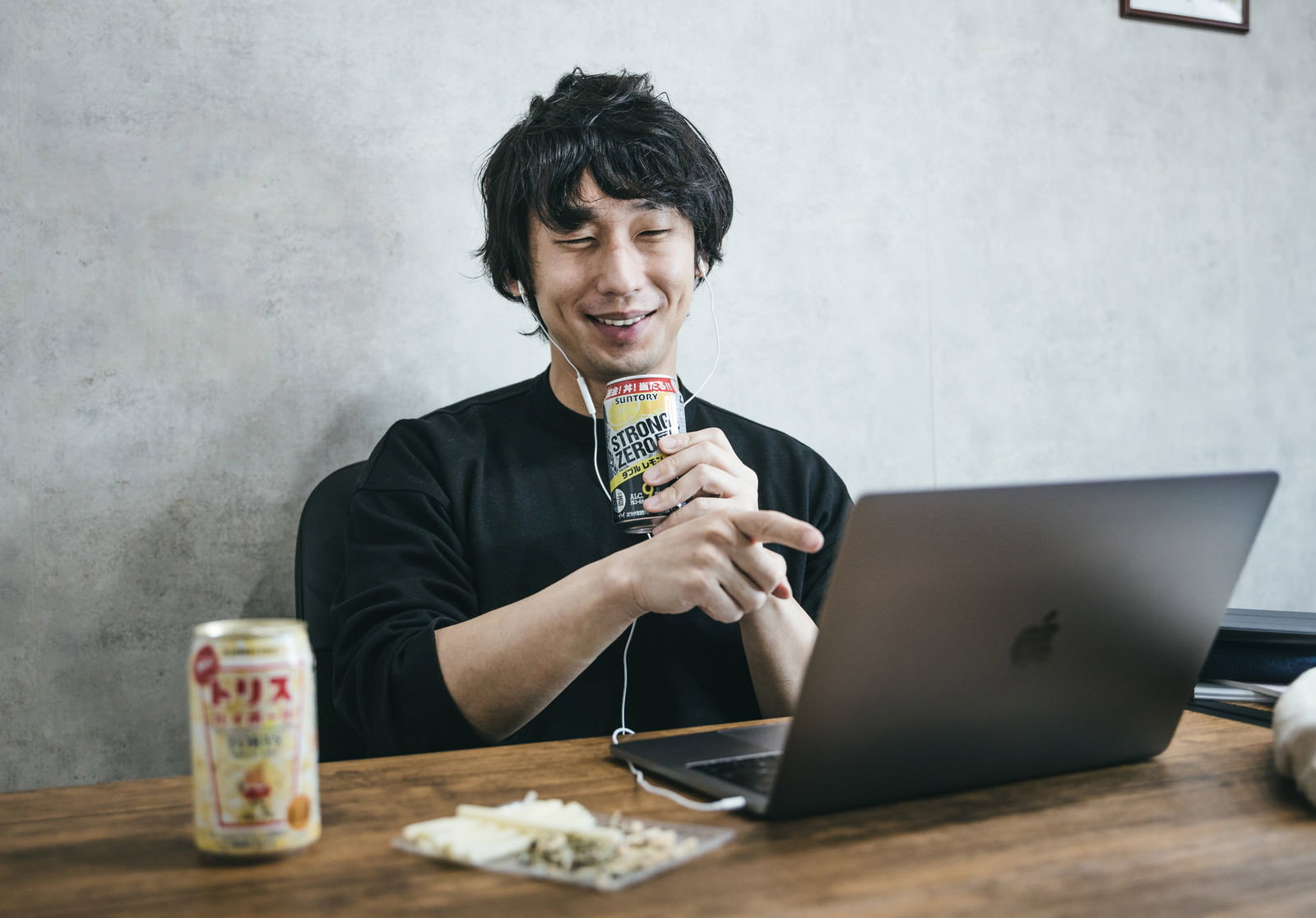 デスクでノートパソコンを開き缶チューハイを持ちながら笑顔でリモート飲みを楽しむ男性［モデル：大川竜弥］