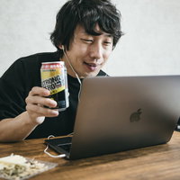 ノートパソコンの前でストロングゼロを手に持ち乾杯する男性の写真