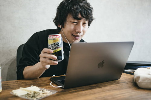 ノートパソコンの前でストロングゼロを手に持ち乾杯する男性