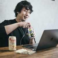 ノートパソコンでボイチャしながらリモート飲みを楽しむ男性エンジニアの写真
