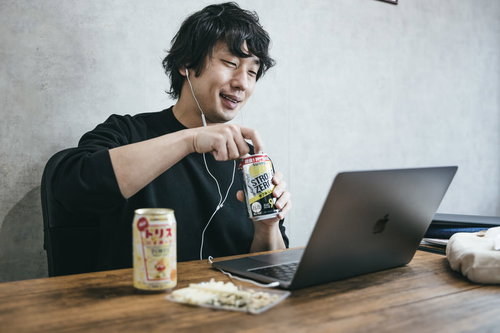 ノートパソコンでボイチャしながらリモート飲みを楽しむ男性エンジニア