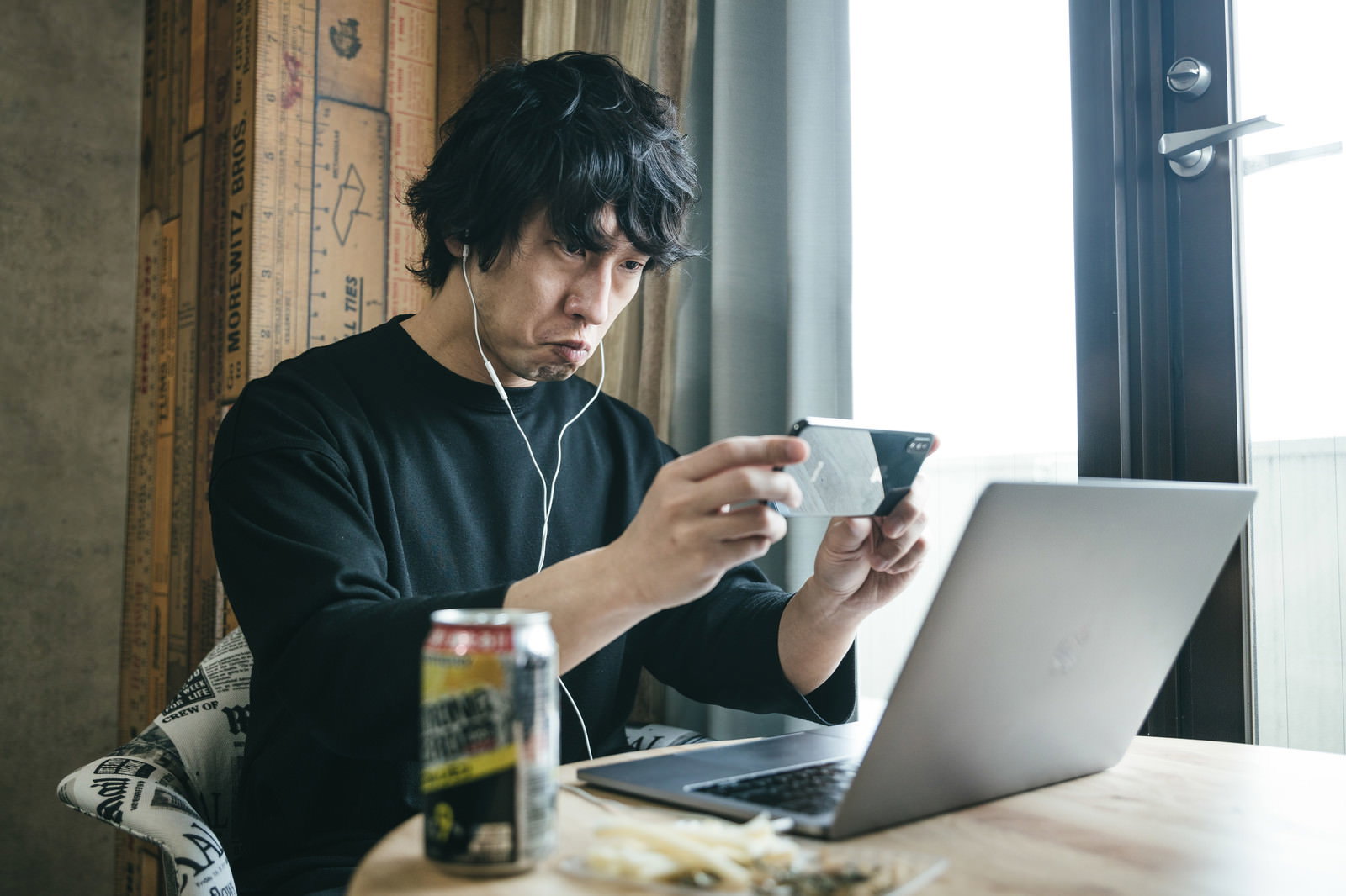 リモート飲み会でスマホを操作する黒いシャツの男性［モデル：大川竜弥］