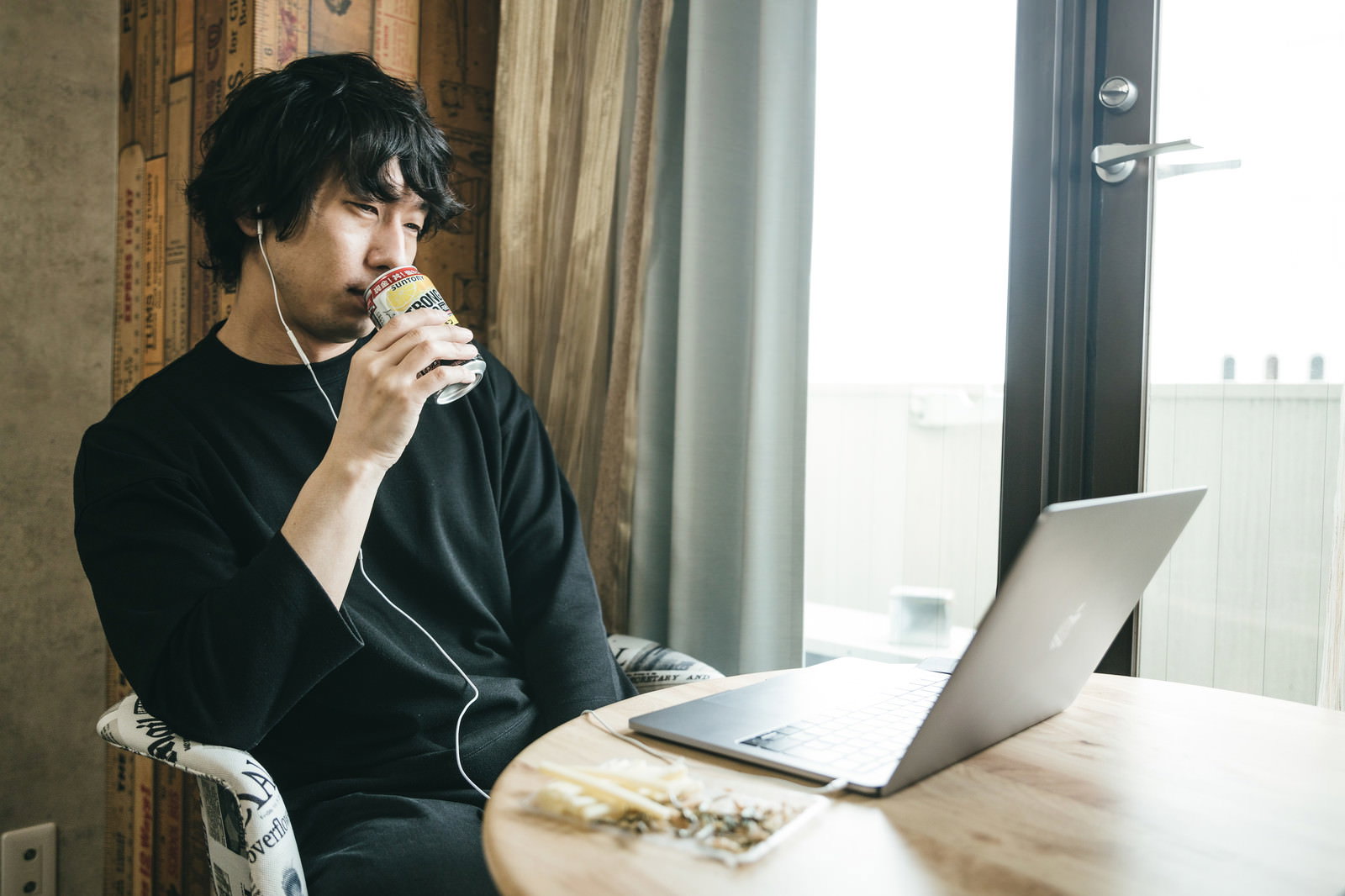 ノートパソコンの前で缶チューハイを飲む黒シャツの男性、下向きの表情［モデル：大川竜弥］