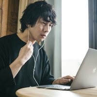 ノートパソコンのリモート会議中に音量を操作する男性の写真