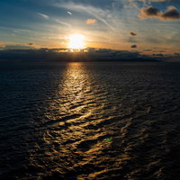 さざ波を照らす夕日の水面、黄昏時の海面風景の写真