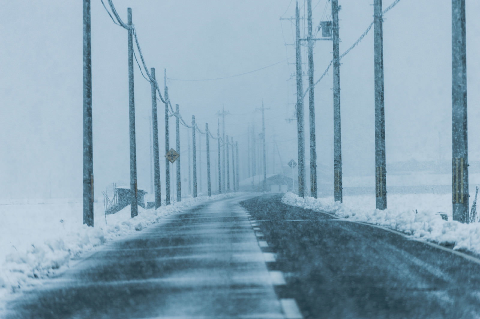 雪に覆われた道路と両脇に立つ電柱が遠方まで続く雪国の冬景色