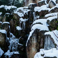 冬の岩場を流れ落ちる水飛沫と積雪の風景の写真