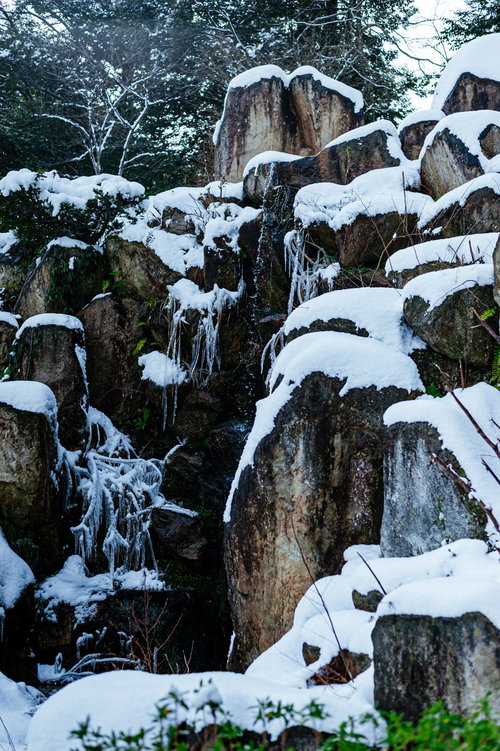 冬の岩場を流れ落ちる水飛沫と積雪の風景