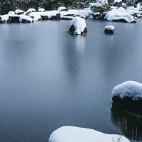 雪が反射して白く映る冬の水面に積もった雪と岩の写真