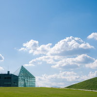 青空の下、緑の丘に建つガラスのピラミッド（モエレ沼公園）の写真