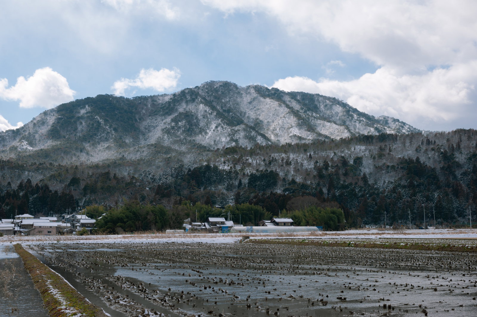 雪が積もった田んぼと雲がかかった山々の冬景色