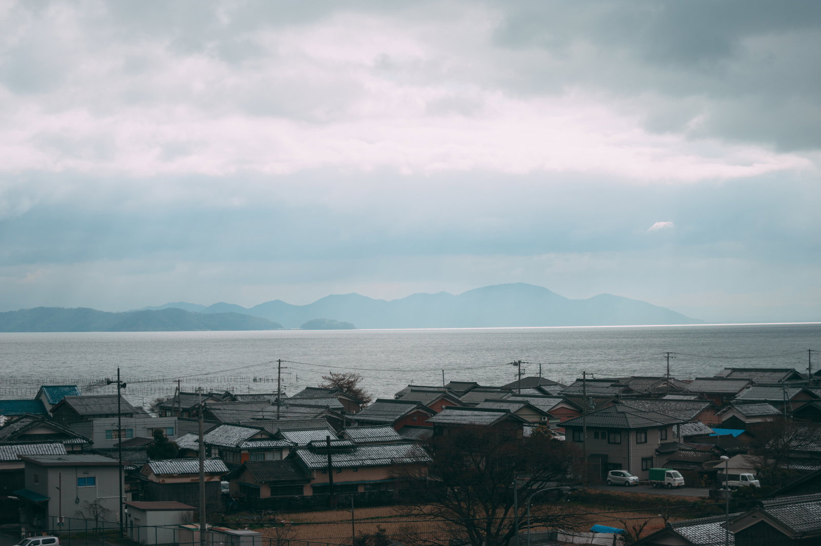 曇り空の下、瓦屋根の住宅街越しに琵琶湖を望む風景
