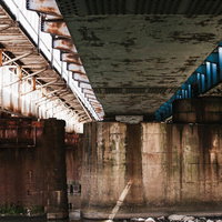 錆びた高架下のコンクリート柱と鉄筋が立ち並ぶ薄暗い空間の写真