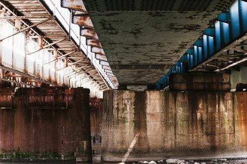 錆びた高架下のコンクリート柱と鉄筋が立ち並ぶ薄暗い空間