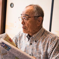 チェック柄シャツを着た高齢男性が眼鏡をかけて新聞を読むの写真