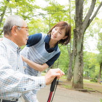 公園のベンチで疲れた表情のお爺さんに声をかける介護士の女性の写真