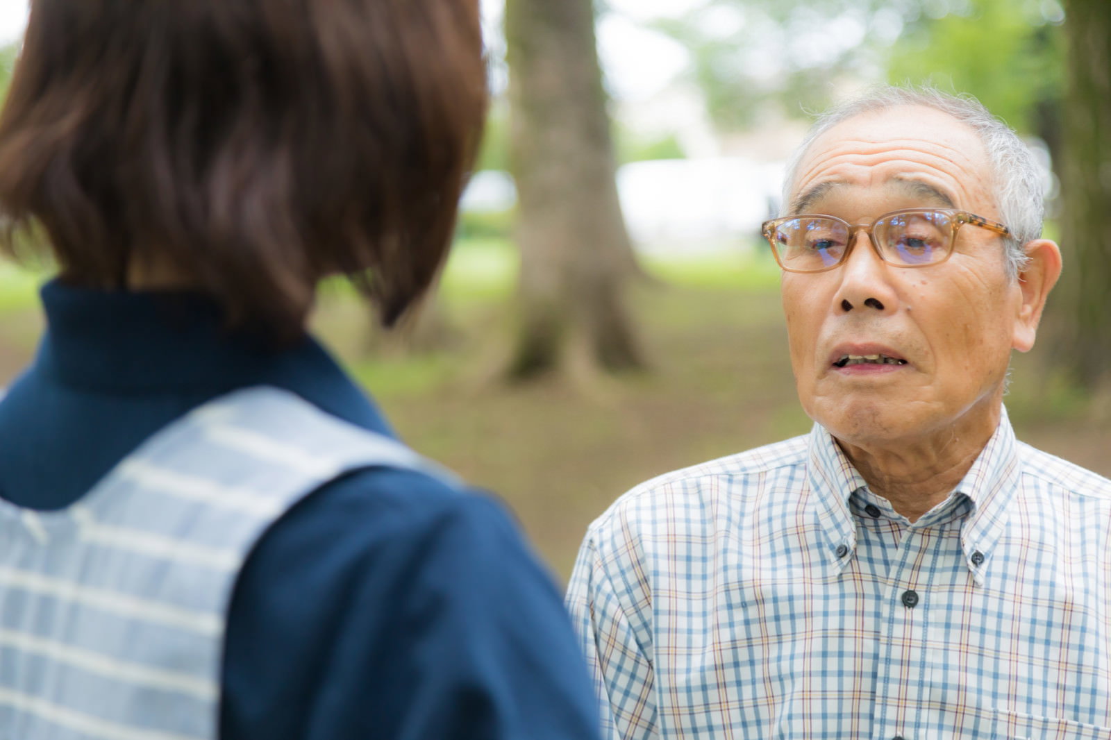 チェック柄のシャツを着た高齢男性と制服姿の女性介護士が向かい合って会話している様子［モデル：まーちゃん yumiko］