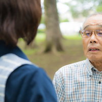 チェック柄シャツの高齢男性と向かい合う介護士の会話の写真