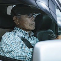 チェック柄のシャツを着た高齢者男性が運転する車の運転席の写真