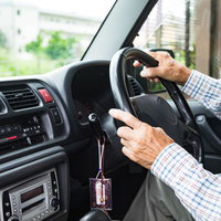 チェック柄シャツを着た高齢者がハンドルを握る運転席の手元の写真