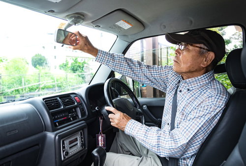 車内でバックミラーを調整する高齢者ドライバー