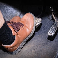 茶色い革靴でブレーキペダルを踏む高齢者の足元の写真