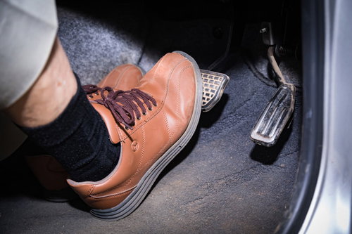 茶色い革靴でブレーキペダルを踏む高齢者の足元