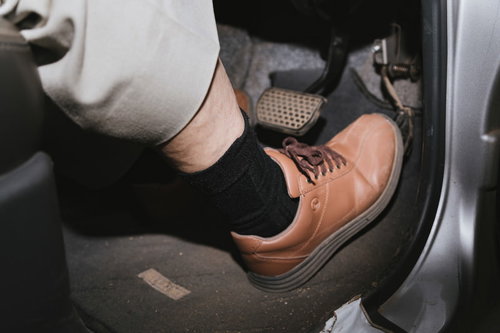 黒い靴を履いてアクセルペダルを踏む高齢者の足元