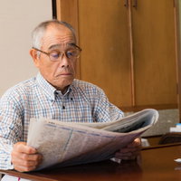 朝刊に目を通す眼鏡をかけたお爺さんが新聞を読むの写真