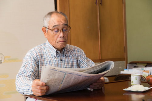 朝刊に目を通す眼鏡をかけたお爺さんが新聞を読む