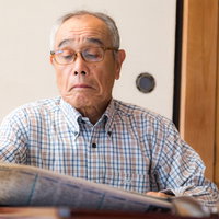 チェック柄のシャツを着たお爺さんが新聞でニュース情報を読むの写真