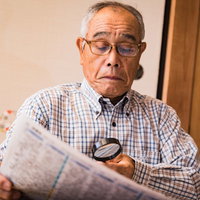拡大鏡で新聞を読む高齢者の男性 朝刊を熟読するシニアの写真