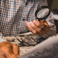 新聞の小さな文字を拡大鏡で読む高齢男性の日常生活の写真