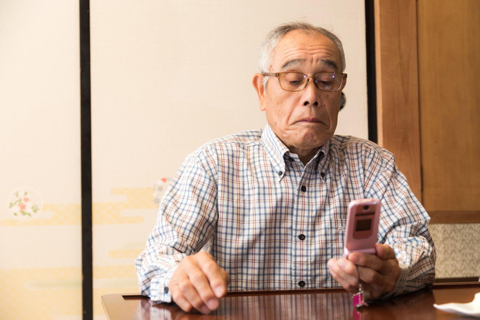 チェック柄のシャツを着て眼鏡をかけた高齢男性がスマートフォンを操作している様子［モデル：まーちゃん］