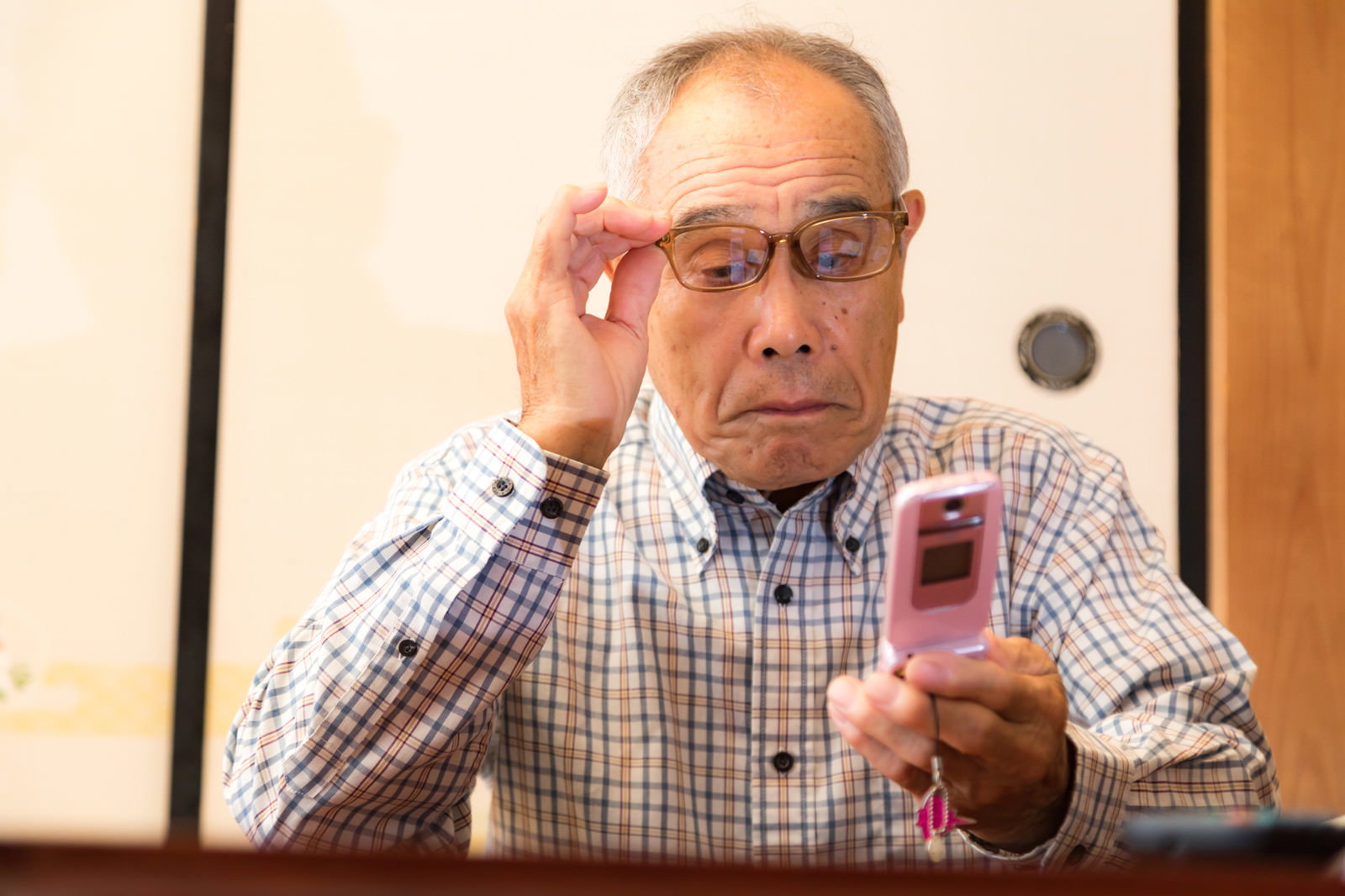 眼鏡をかけたシニア男性が携帯電話を見て驚いている様子［モデル：まーちゃん］