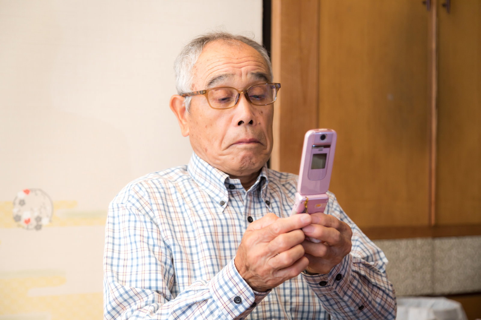 眼鏡をかけたお爺さんが携帯電話を手に持ち、画面を見ながら返事をしている［モデル：まーちゃん］