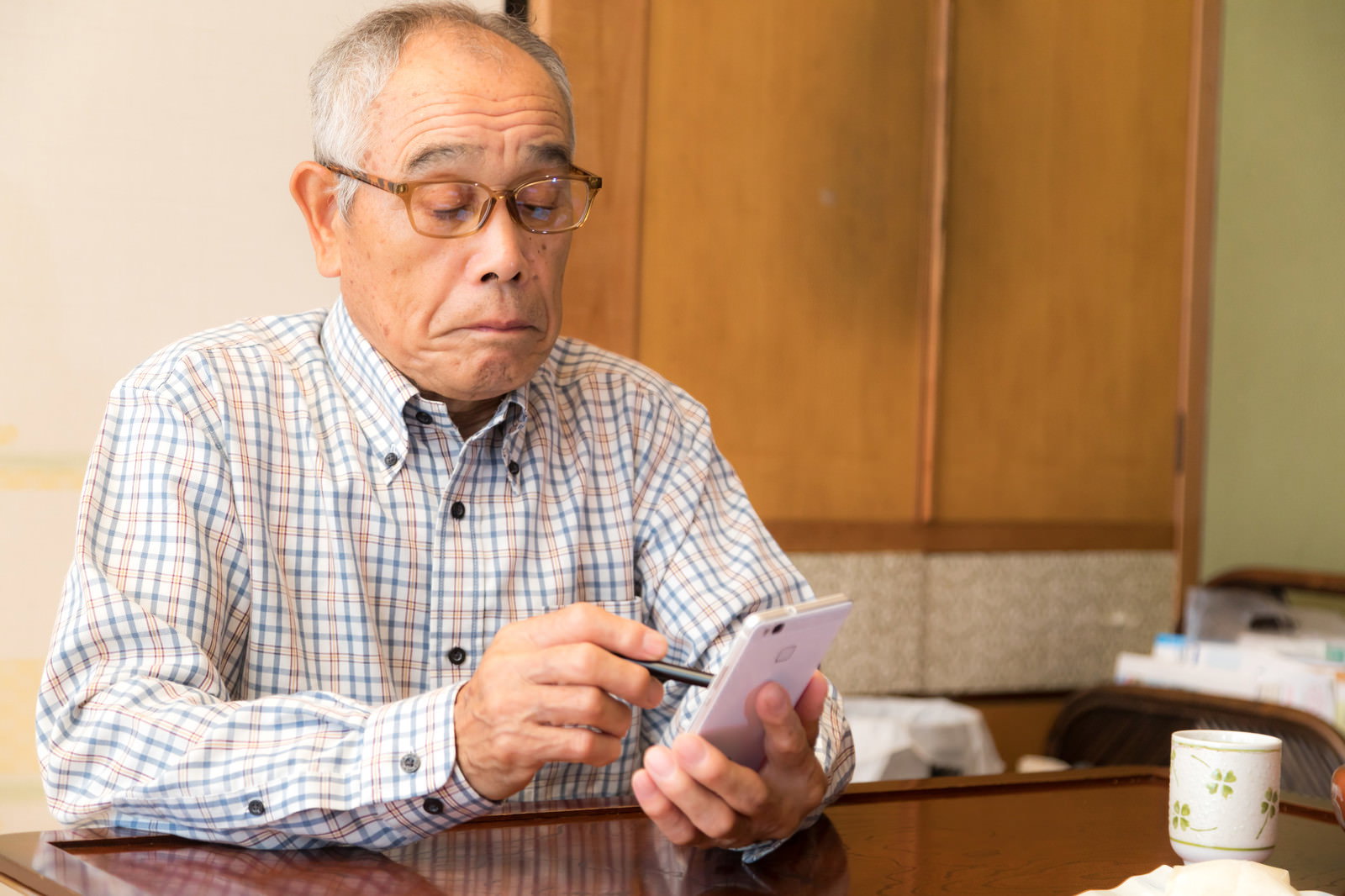 眼鏡をかけたシニア男性が室内でスマートフォンを操作している［モデル：まーちゃん］