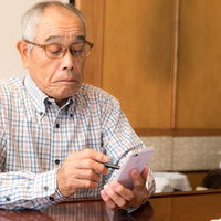 慣れない手つきでスマホを操作する高齢のお爺さんの写真