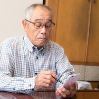 スマートフォンを手に持ち画面を見るスマホ初心者の高齢者の写真