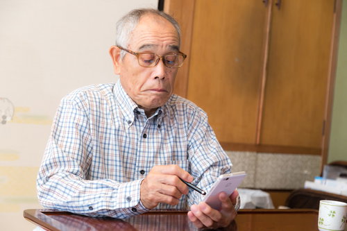 スマートフォンを手に持ち画面を見るスマホ初心者の高齢者