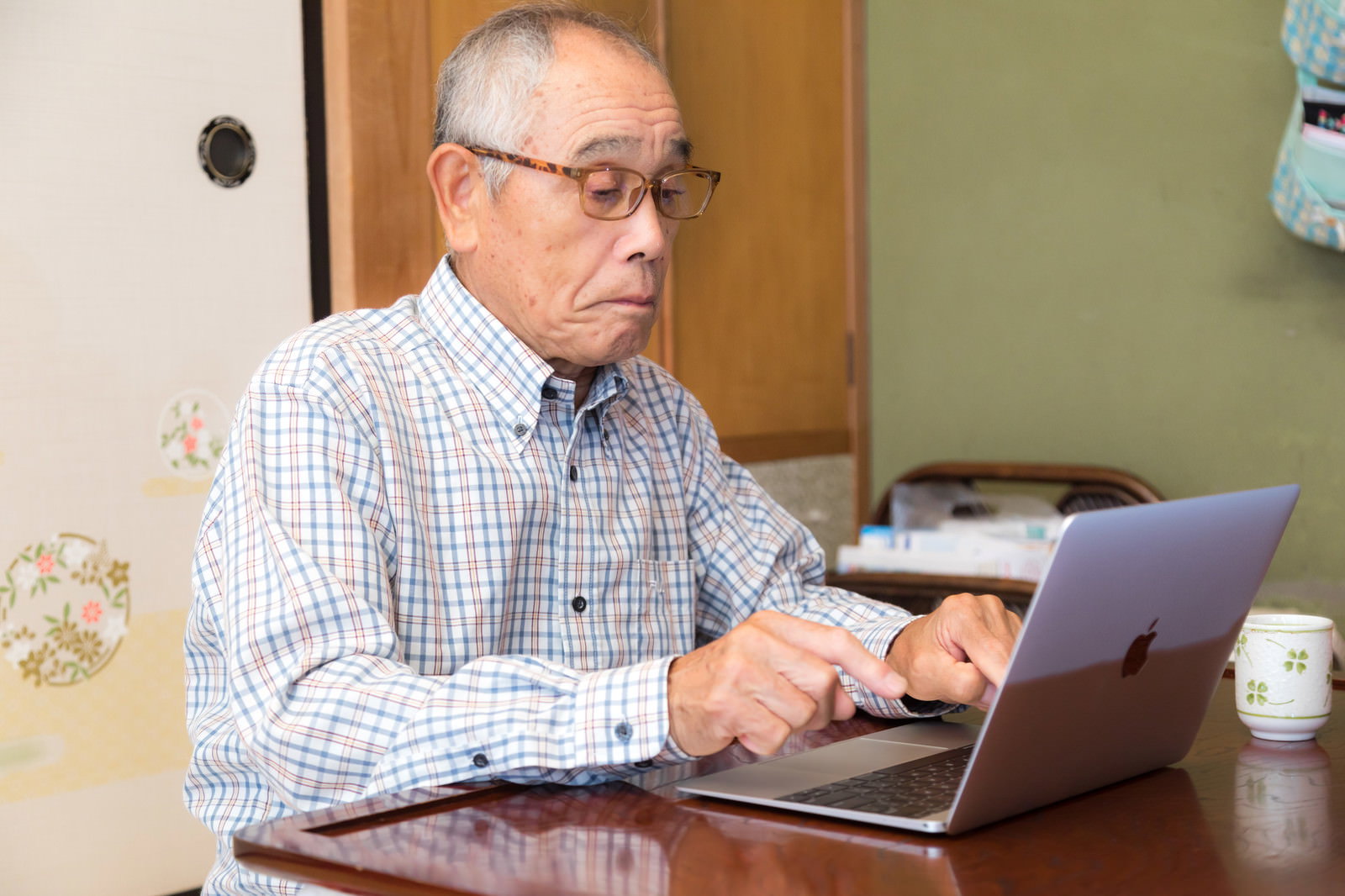 高齢男性が自宅でMacBookを一本指で操作している［モデル：まーちゃん］