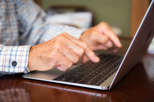 チェック柄シャツの男性がノートパソコンを一本指でタイピング