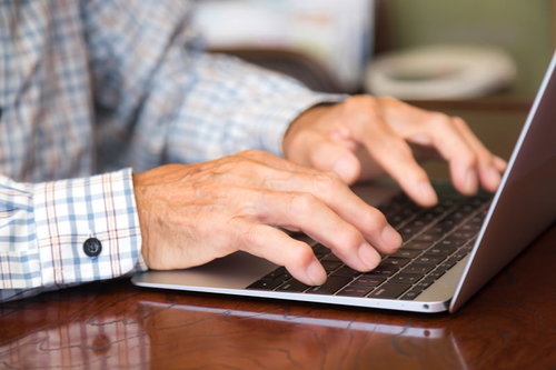 チェック柄シャツを着た高齢者が慣れた手つきでキーボードをタイピングする手元